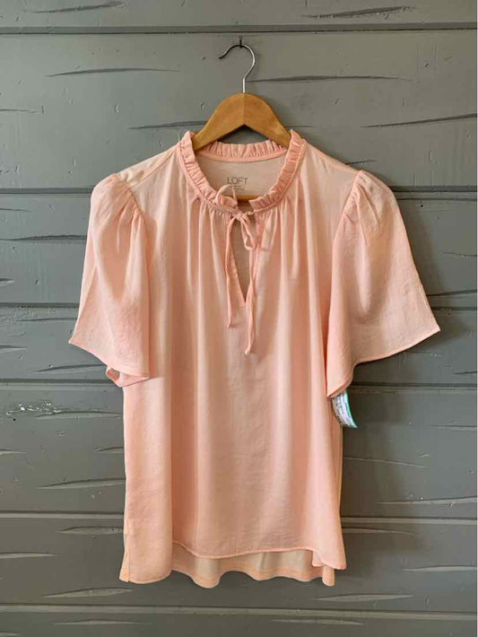 Light pink short-sleeve blouse with gathered neckline and tie detail on wooden hanger.