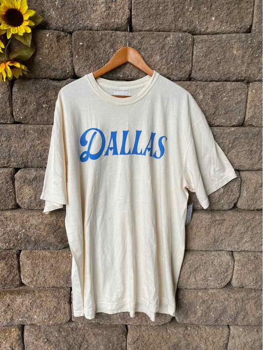 Off-white oversized cotton T-shirt with blue "DALLAS" text and short sleeves on wooden hanger.