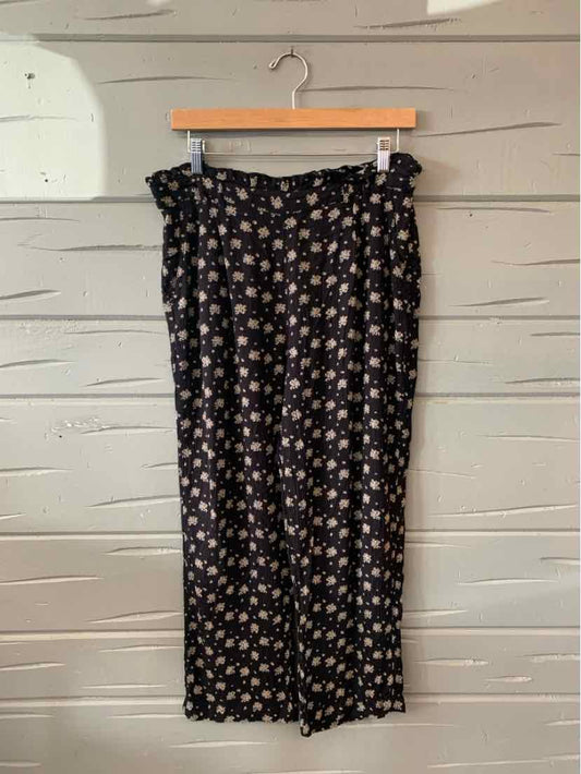 Black wide-leg pants with small white and beige floral print and elastic waistband hanging on wooden hanger.