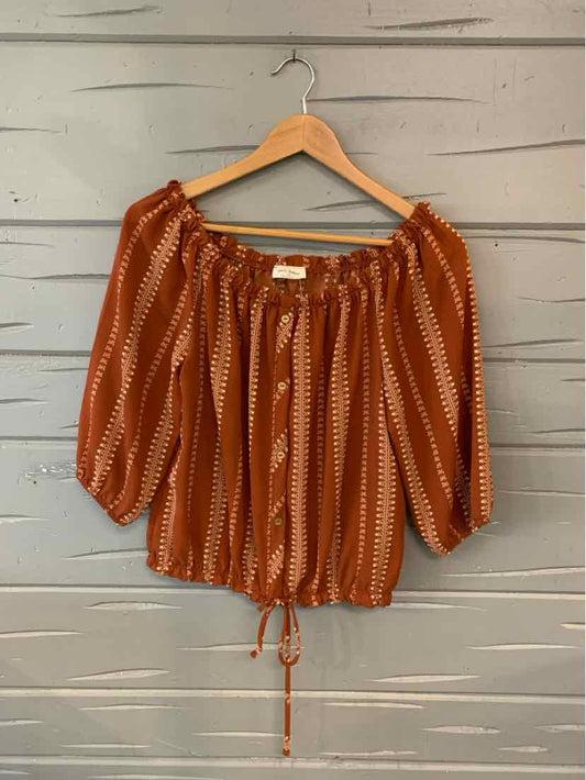 Rust orange off-shoulder blouse with white geometric stripes and drawstring hem on wooden hanger.