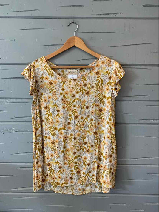 Light yellow short-sleeve blouse with floral print and scoop neckline hanging on wooden hanger.