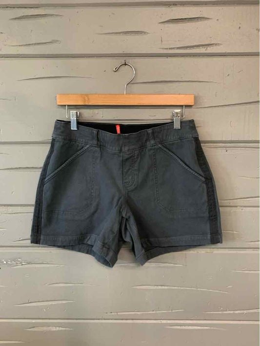 Gray mid-rise shorts with front pockets and a fitted waist hanging on a wooden hanger against a light wooden wall.