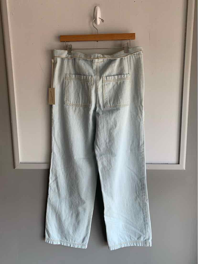 Light wash denim jeans with wide legs and back patch pockets hanging on wooden hanger.