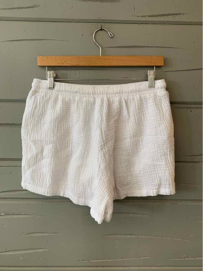 White textured cotton shorts with elastic waistband and relaxed fit hanging on wooden hanger.