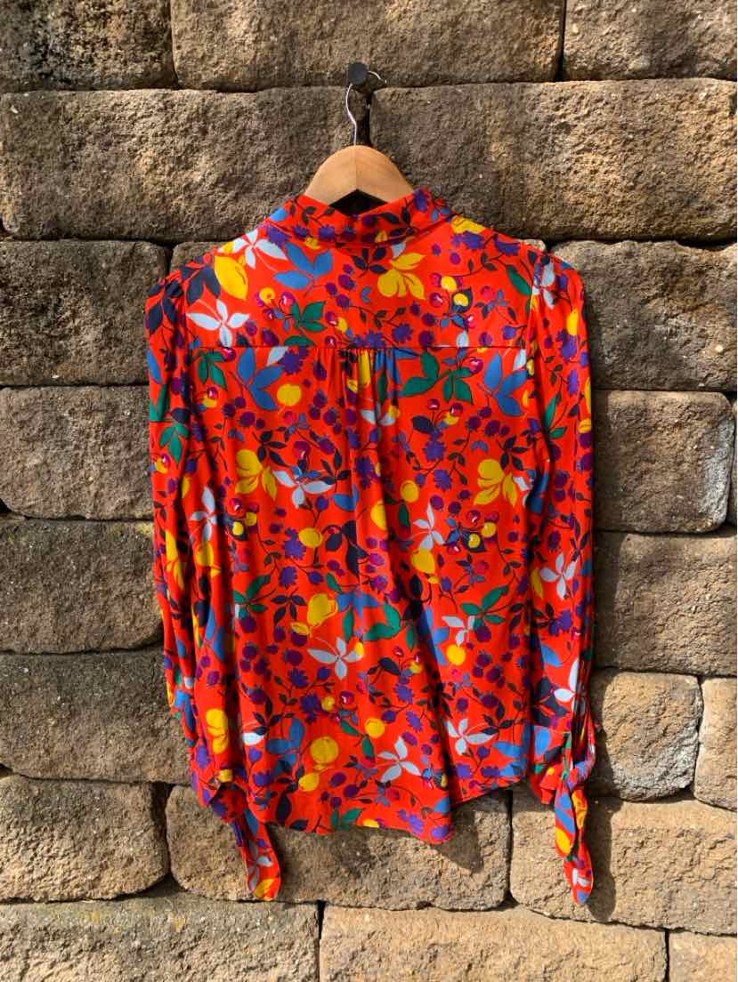 Red floral long-sleeve blouse with multicolor flowers and tie-detail cuffs hanging on wooden hanger.