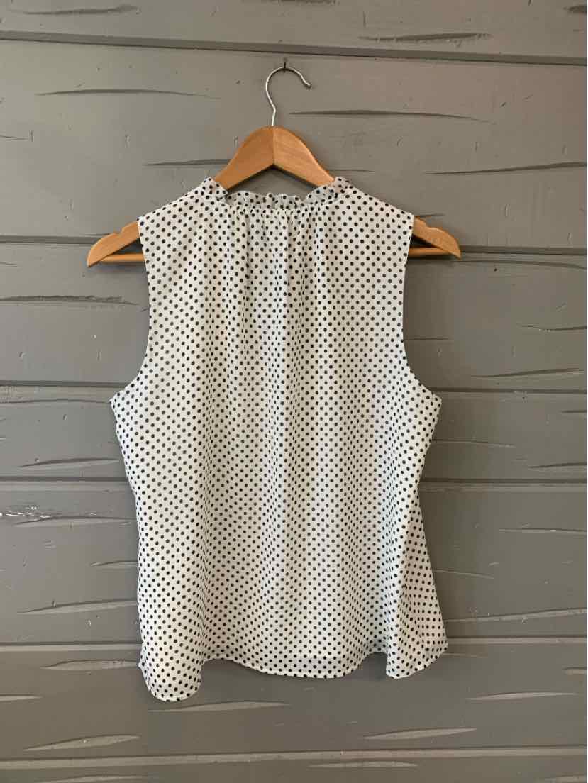White sleeveless blouse with black polka dots and a keyhole back detail on wooden hanger.