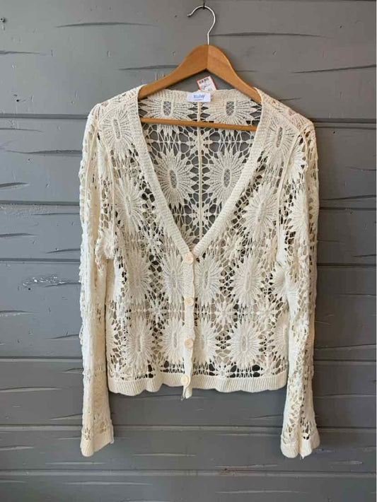 Cream-colored crochet cardigan with floral patterns, long sleeves, and a V-neckline on wooden hanger.