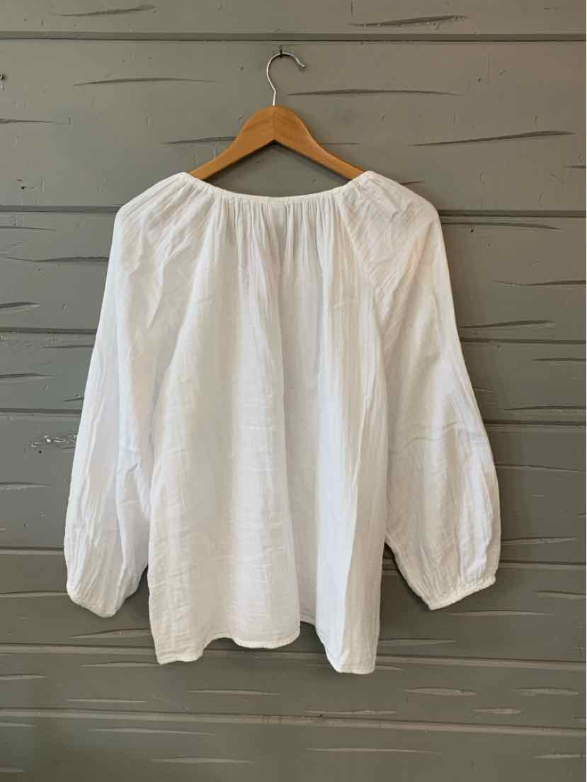 White long-sleeve blouse with gathered neckline and elastic cuffs hanging on wooden hanger.