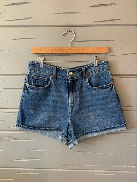 Blue denim high-waist shorts with front button and zipper closure hanging on wooden hanger.