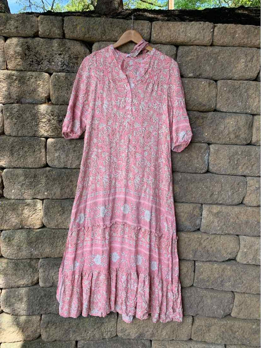 Pink floral midi dress with long sleeves and tiered skirt hanging on wooden hanger.