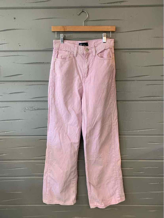 Light lavender high-waisted wide-leg jeans with front pockets and belt loops hanging on wooden hanger against gray wooden.