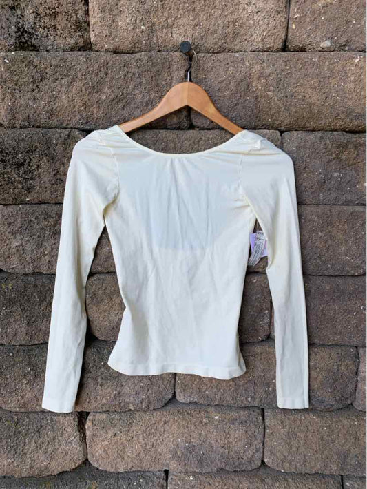 Off-white long-sleeve fitted top with scoop neckline and soft, lightweight fabric hanging on wooden hanger against stone.