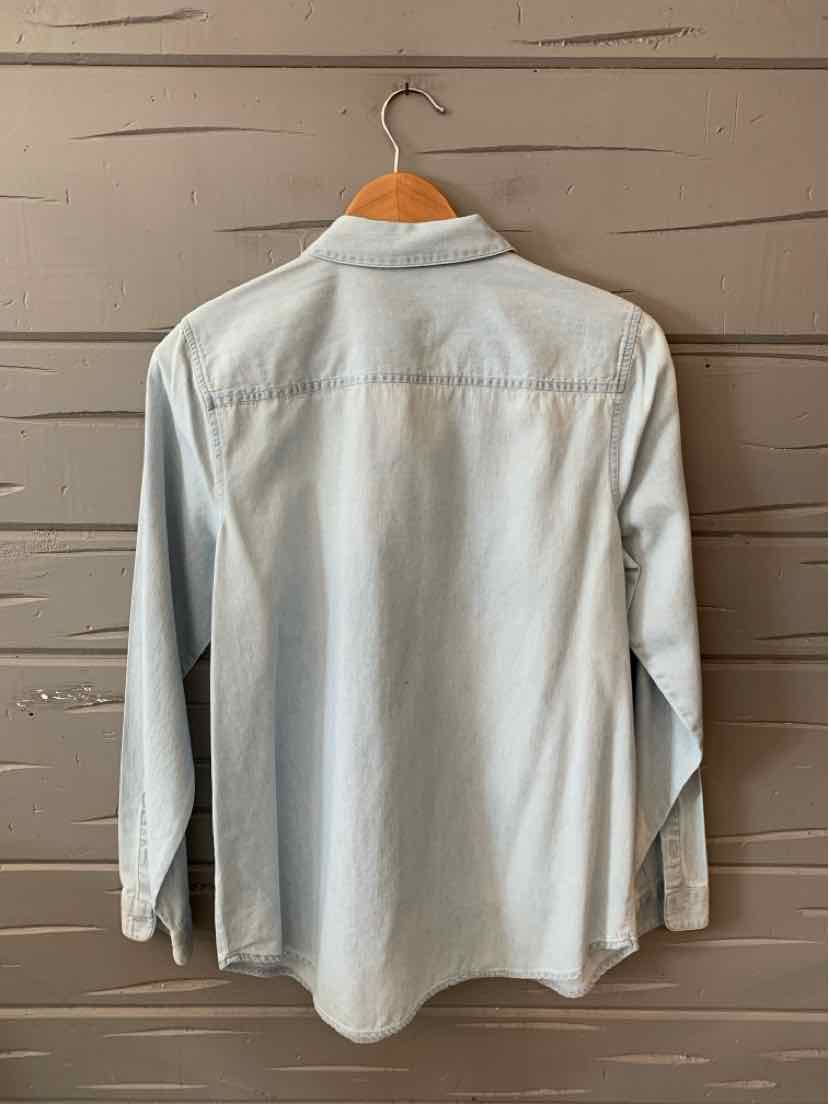 Light blue denim long-sleeve shirt with button cuffs and a classic collar hanging on wooden hanger.