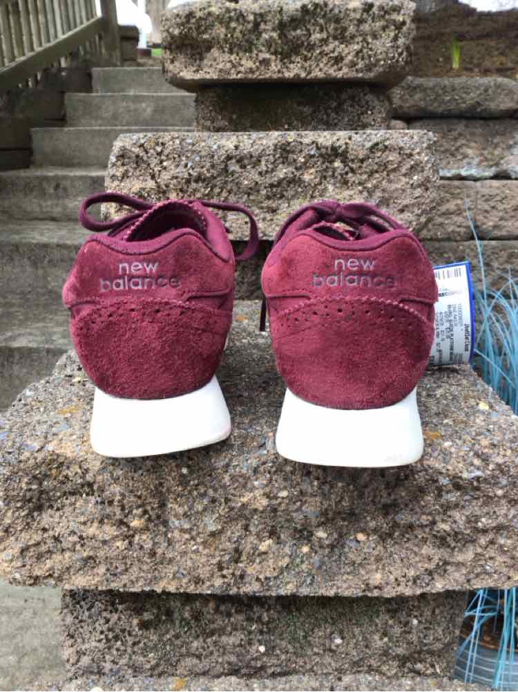 Pair of burgundy suede New Balance sneakers size 7 with white soles viewed from the back on stone steps.