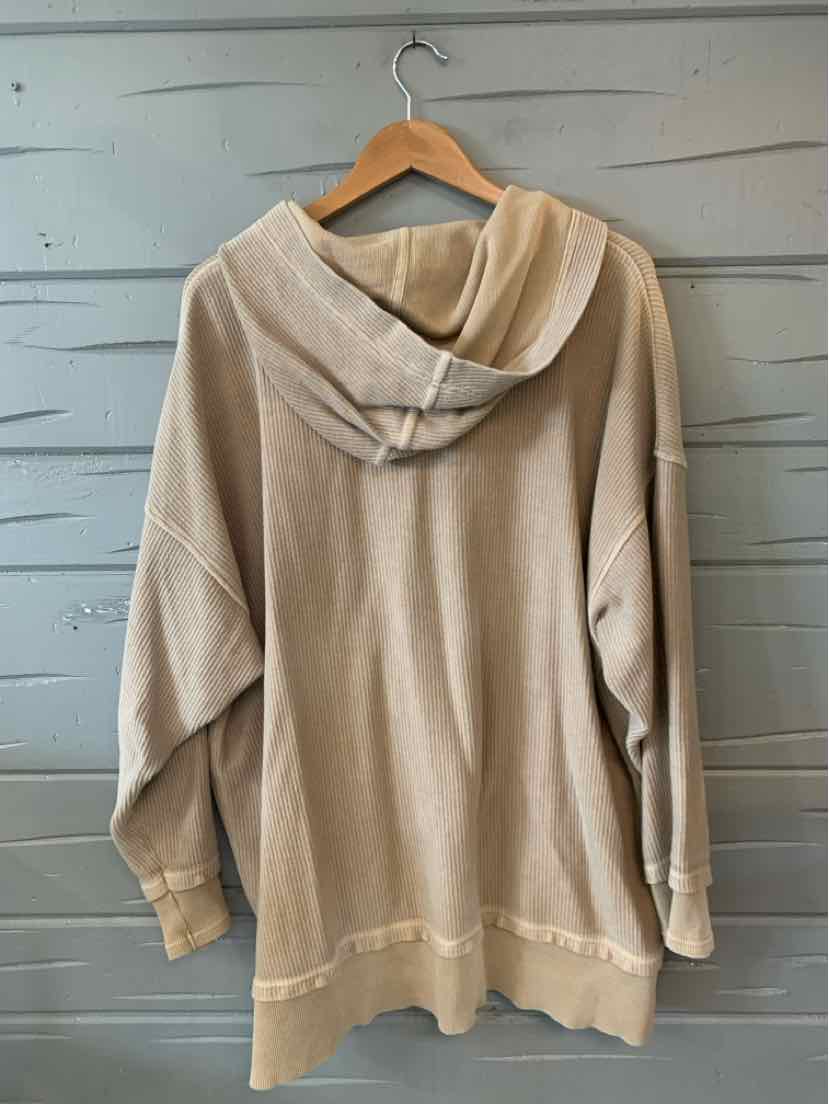 Oversized tan hoodie with front pocket and ribbed cuffs, hanging on wooden hanger.