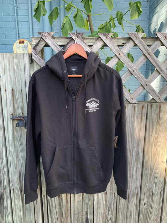 Black Vans hoodie with half-zip front and white logo on left chest, hanging on wooden fence.