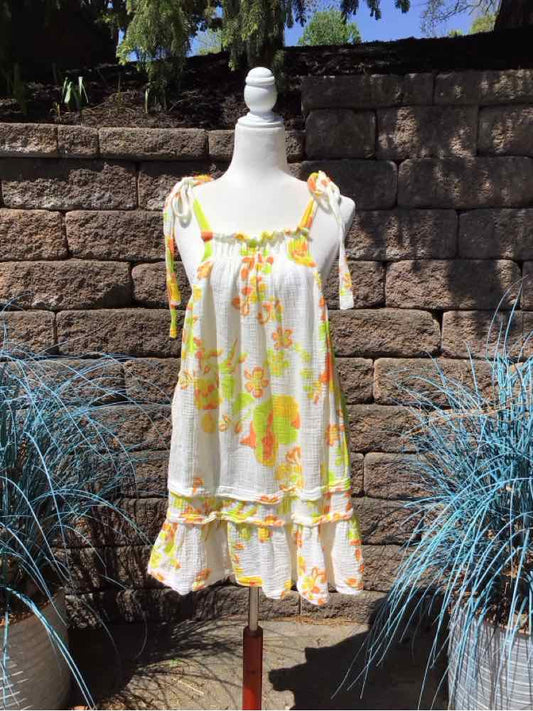 White dress with yellow and orange floral print, ruffled hem, and tied shoulder straps on mannequin.