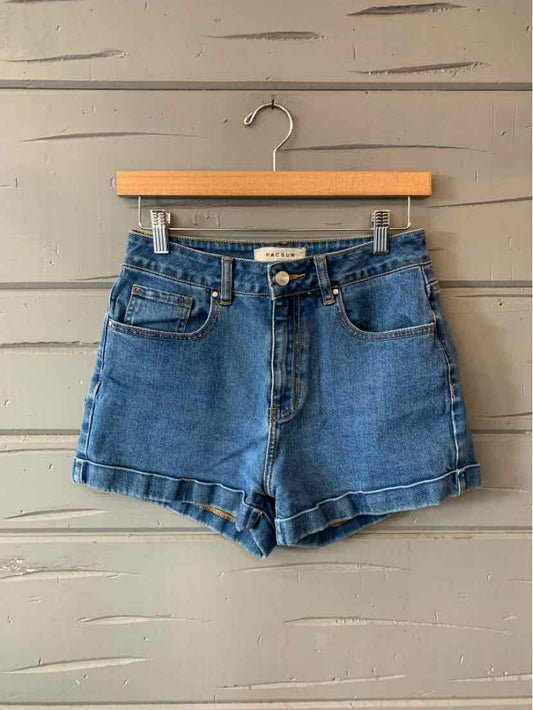 Blue denim women's shorts with front pockets and button closure hanging on wooden hanger.