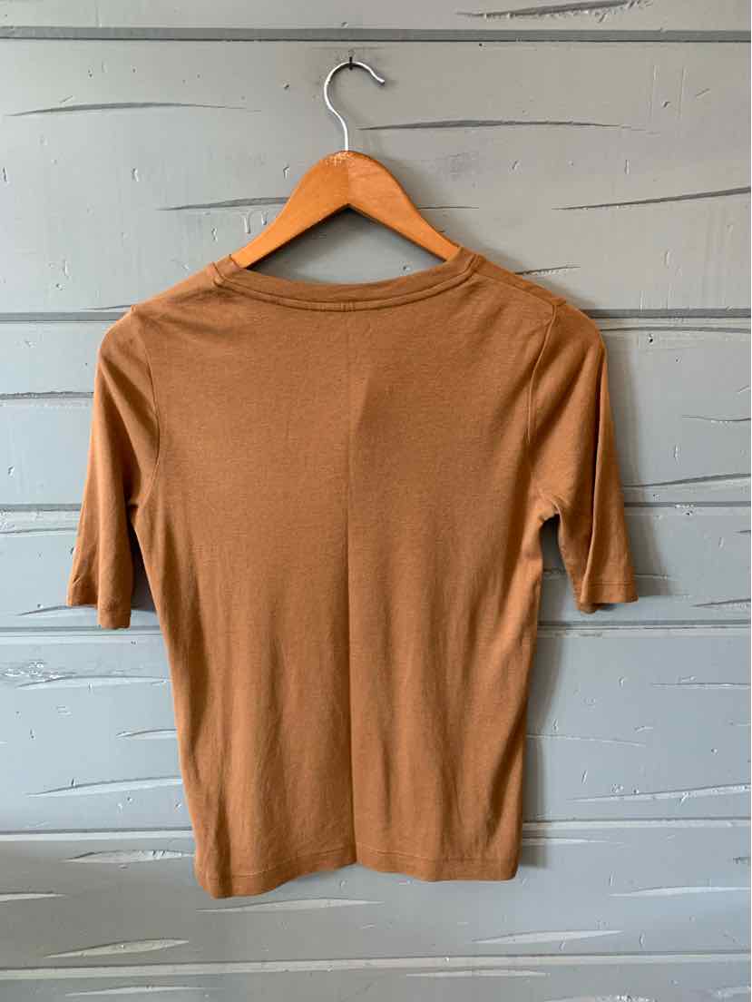 Tan short-sleeve knit top with crew neckline on wooden hanger against gray wooden background.
