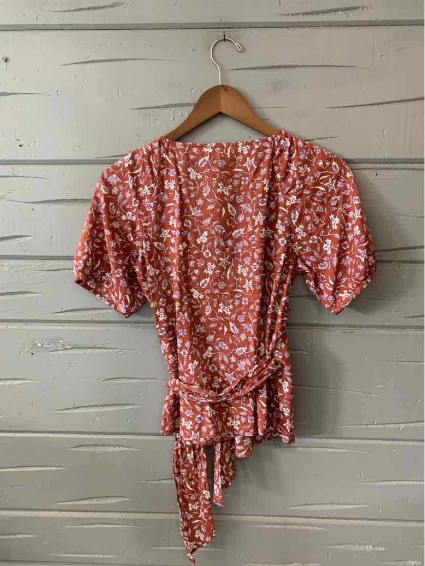 Rust-colored short-sleeve blouse with white floral pattern and side tie detail.