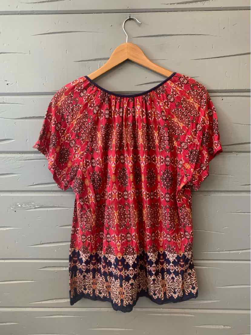 Red paisley patterned blouse with short sleeves and gathered neckline hanging on wooden hanger.