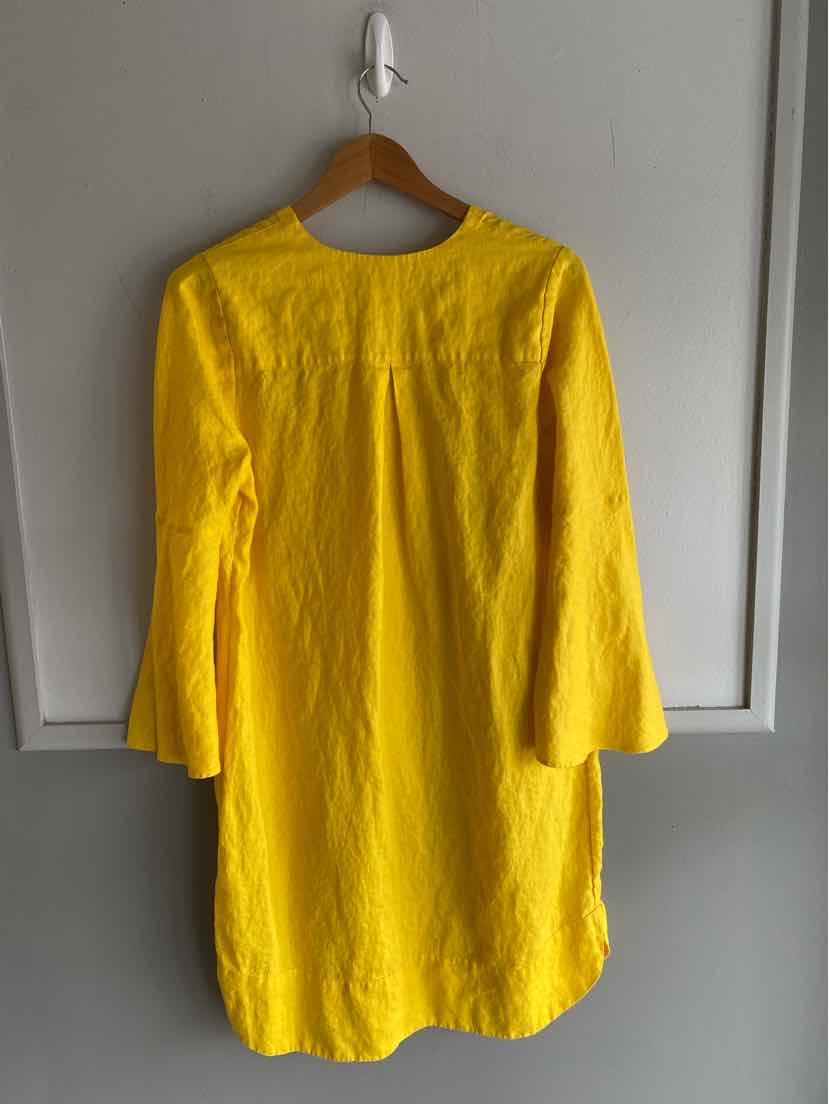 Yellow long-sleeve tunic dress with round neckline in medium size hanging on wooden hanger.