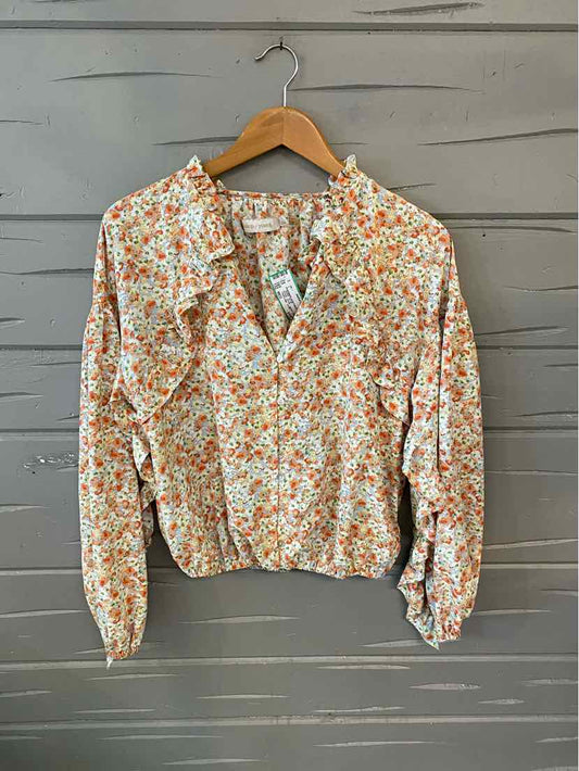 Long-sleeve blouse with orange and green floral print on white fabric, collared with button-down front.