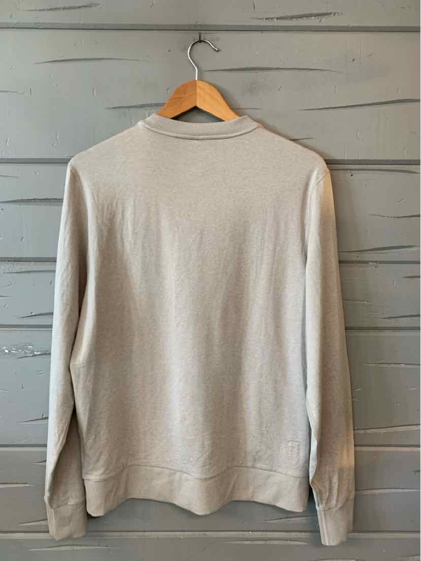 Beige long-sleeve crewneck sweatshirt with ribbed cuffs and hem hanging on wooden hanger.