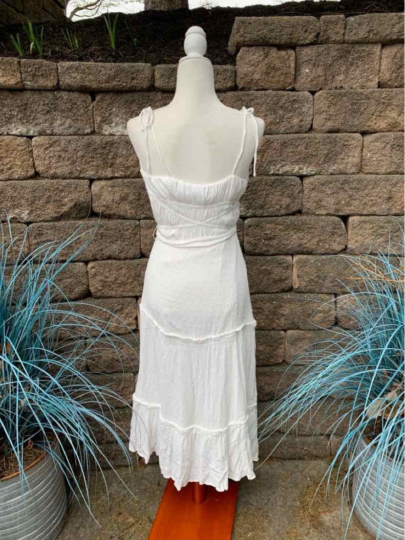 White sleeveless dress with thin straps and tiered ruffle hem on mannequin against stone wall.