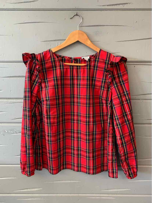 Red plaid long-sleeve blouse with ruffle shoulder details and a round neckline on wooden hanger.