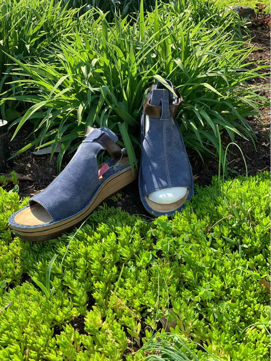 Blue leather open-toe wedge sandals with ankle strap and cork sole on grass background.