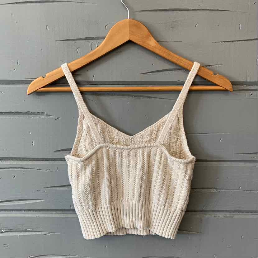 Tan ribbed knit cropped tank top with thin adjustable straps on wooden hanger.