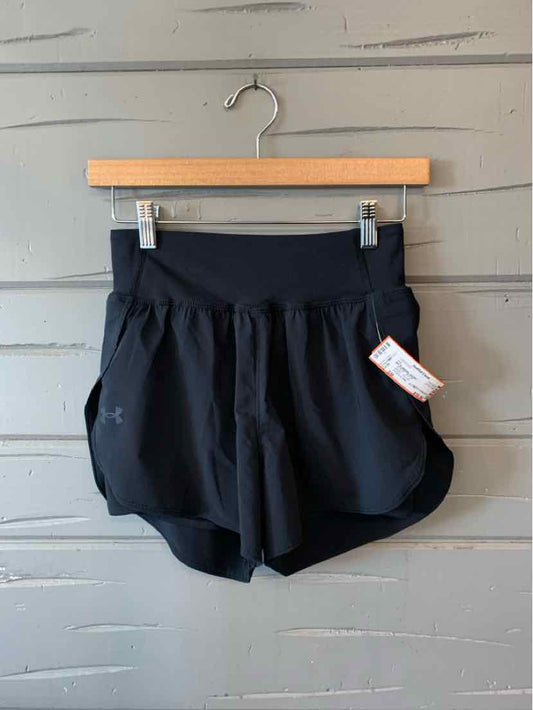 Black athletic shorts with wide waistband and small Under Armour logo on left leg hanging on wooden hanger.