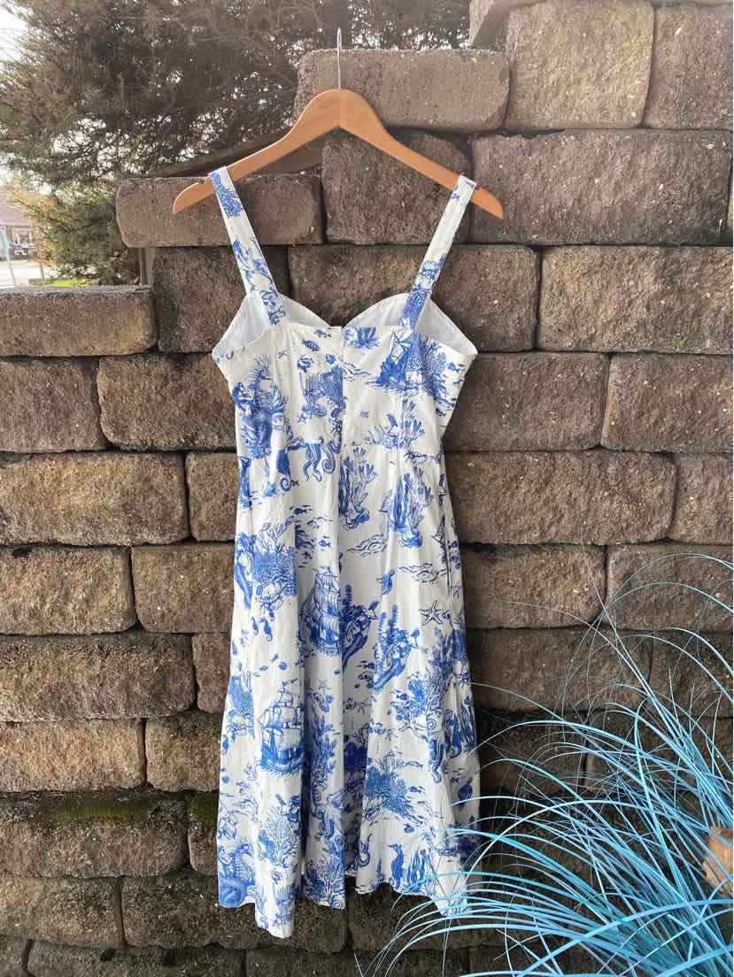 White midi dress with blue floral print, adjustable straps, and fitted bodice hanging on wooden hanger.