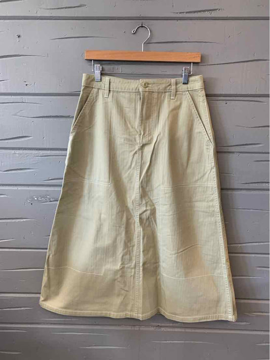Beige wide-leg skirt with belt loops and front pockets hanging on wooden hanger against gray wooden wall.