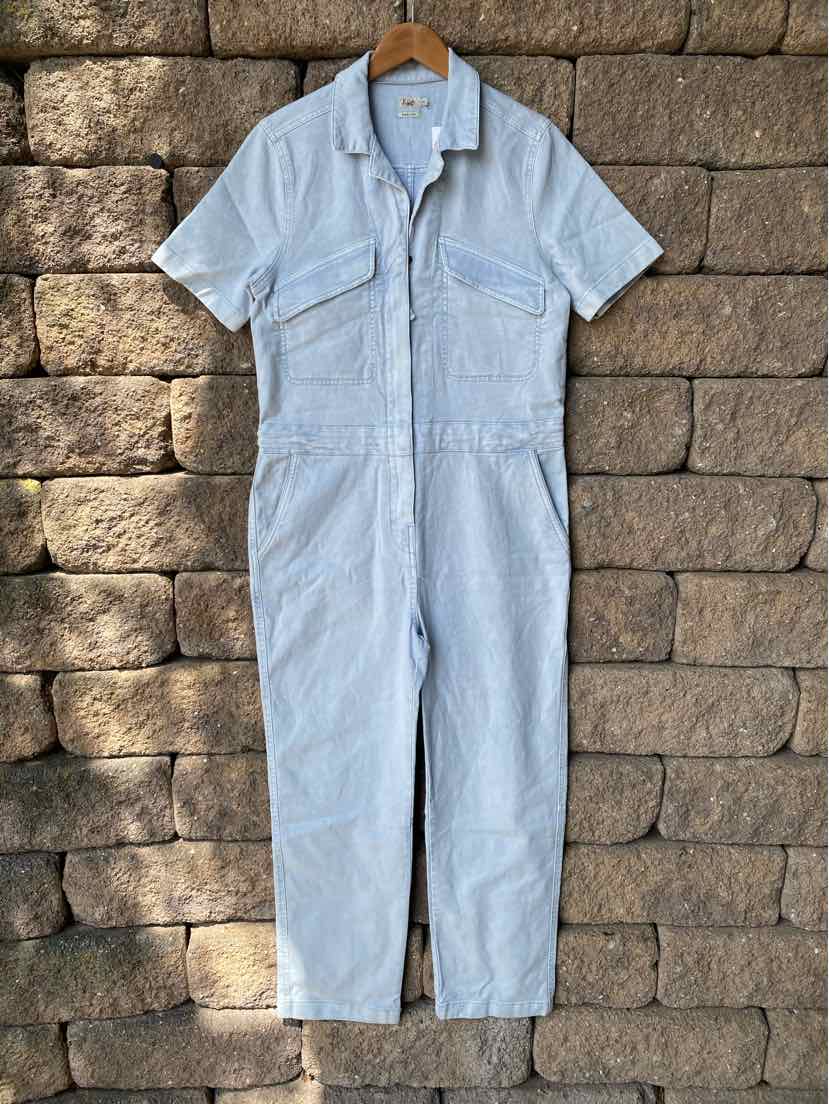 Light blue short-sleeve jumpsuit with front pockets and a collar, hanging on a wooden hanger.