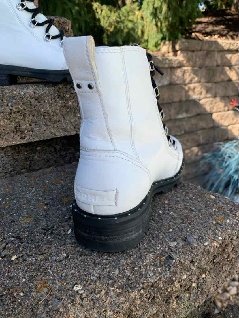 White leather Sorel ankle boot with a pull tab, side buckle detail, and thick black sole.