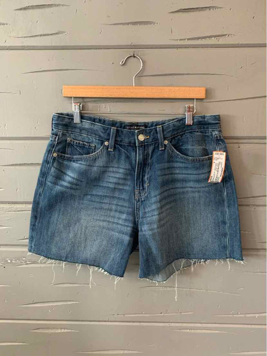 Blue denim shorts with frayed hems and five-pocket styling hanging on wooden hanger.
