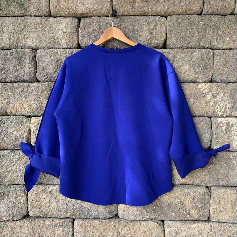 Royal blue long-sleeve blouse with tie cuffs and a relaxed fit on wooden hanger.