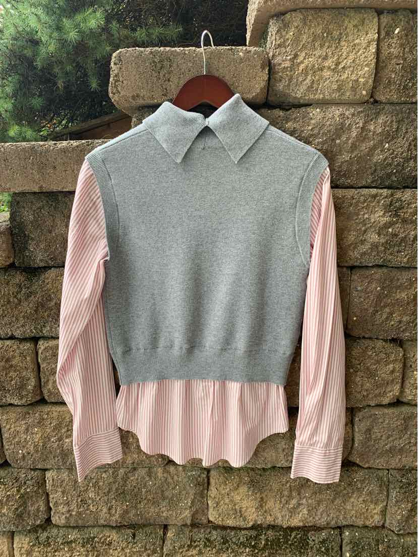 Gray sleeveless knit vest layered over pale pink long-sleeve collared shirt with button cuffs.