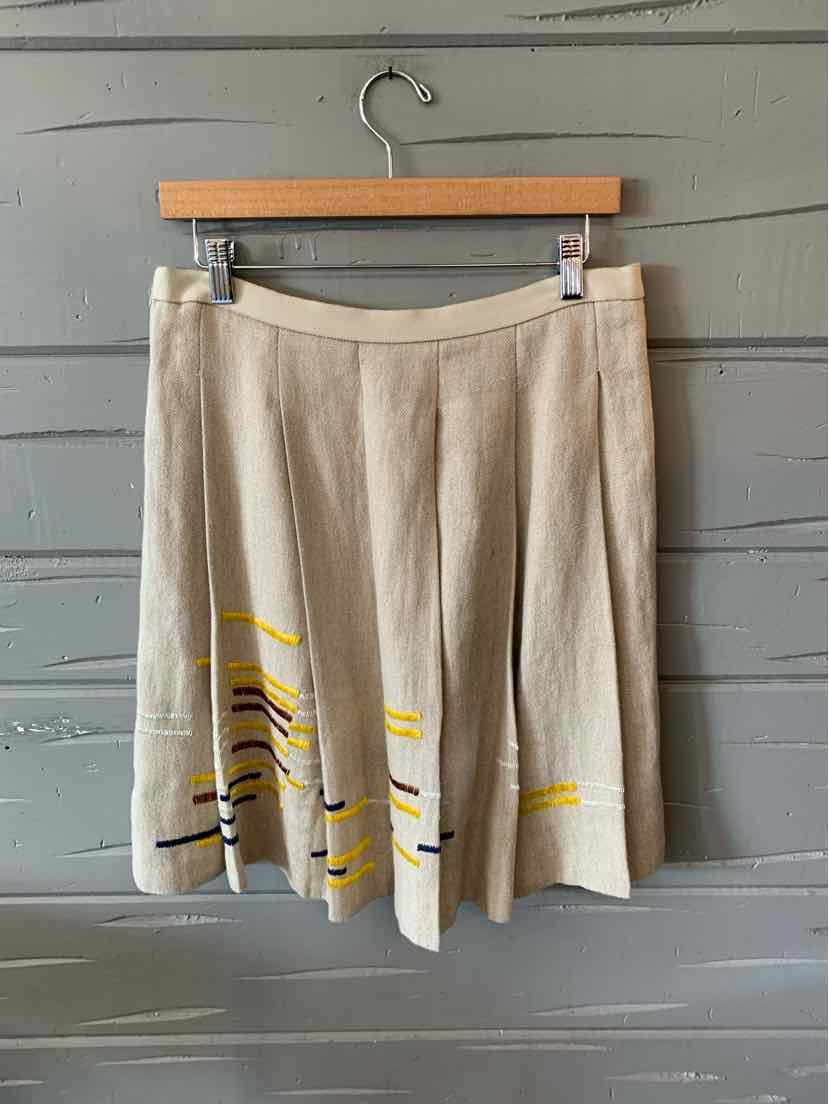 Tan pleated skirt with yellow, black, and white abstract stripe details near the hem, size 6.