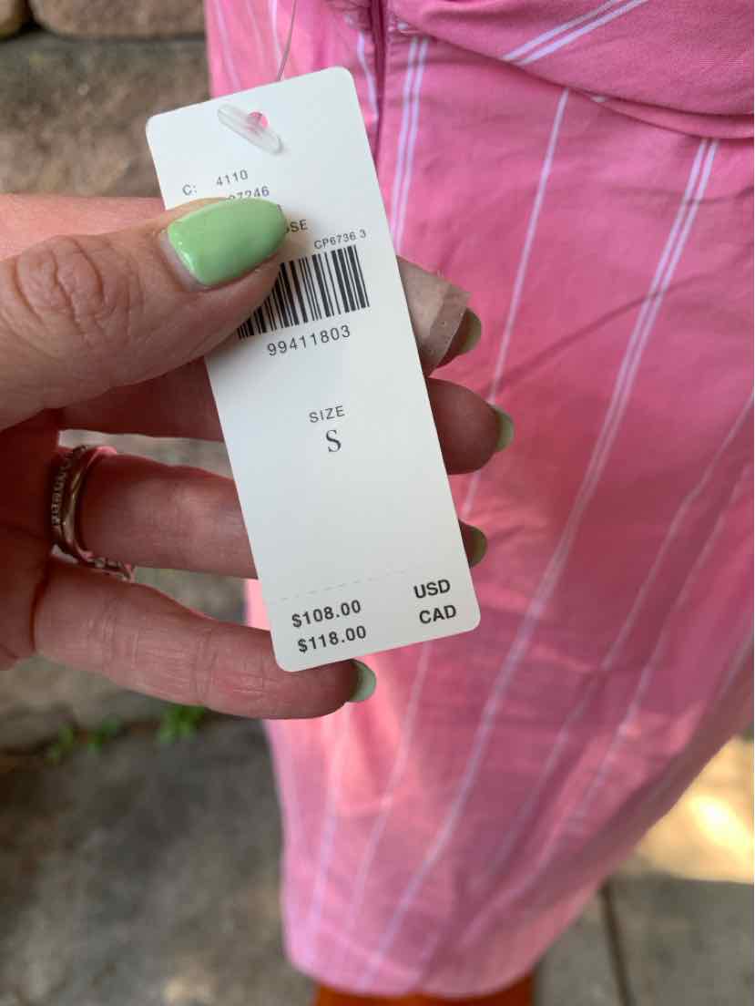 Pink skirt with white vertical and horizontal stripes in a small size tag held by a hand with green nail polish and rings.
