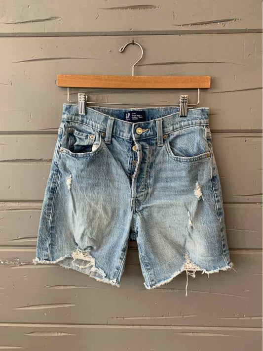 Light blue distressed denim shorts with frayed hems and multiple pockets hanging on wooden hanger.