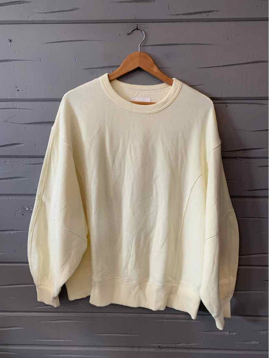 Cream-colored oversized sweatshirt with long puffed sleeves and ribbed cuffs and hem hanging on wooden hanger.