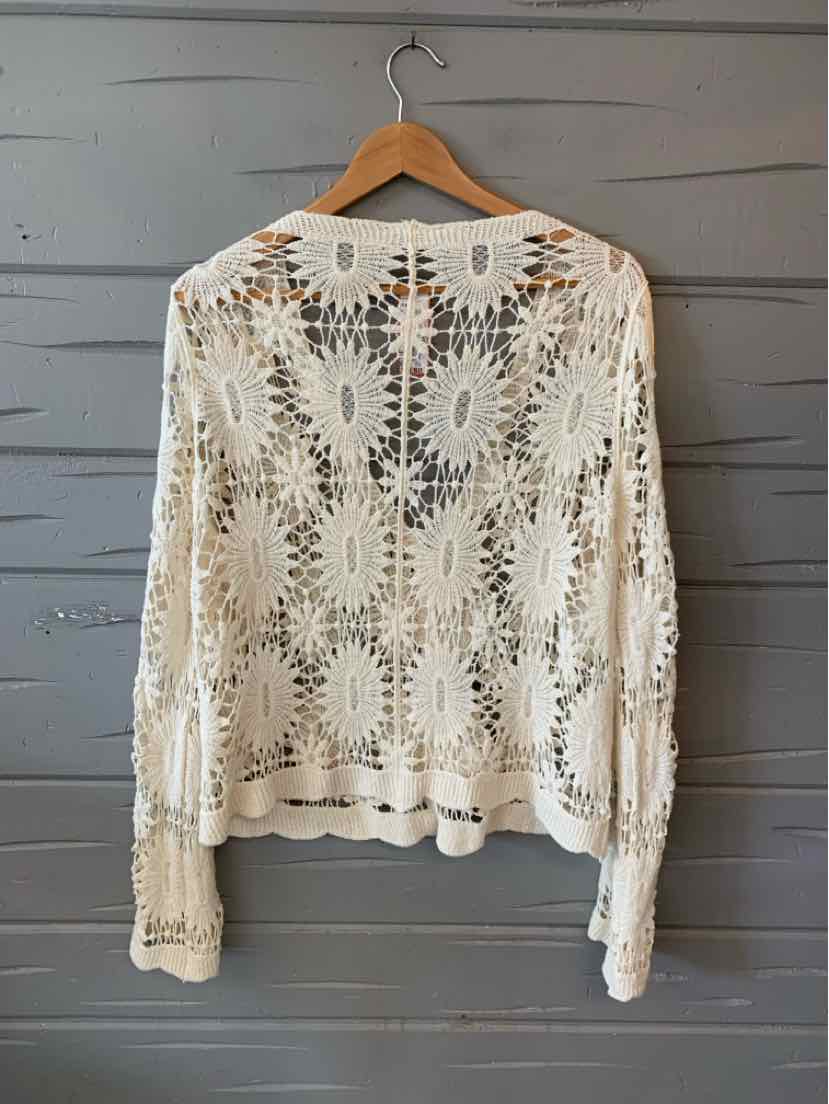 White crochet long-sleeve top with intricate floral patterns, hanging on wooden hanger.