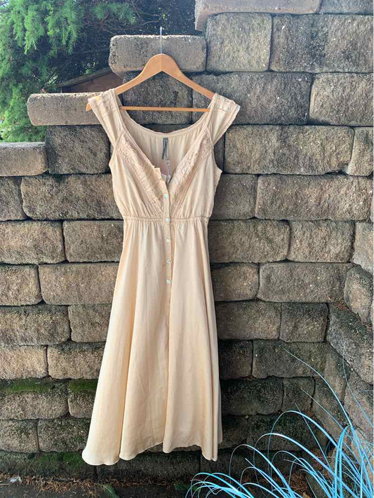 Tan sleeveless midi dress with V-neckline, button front, and fitted waist on wooden hanger.