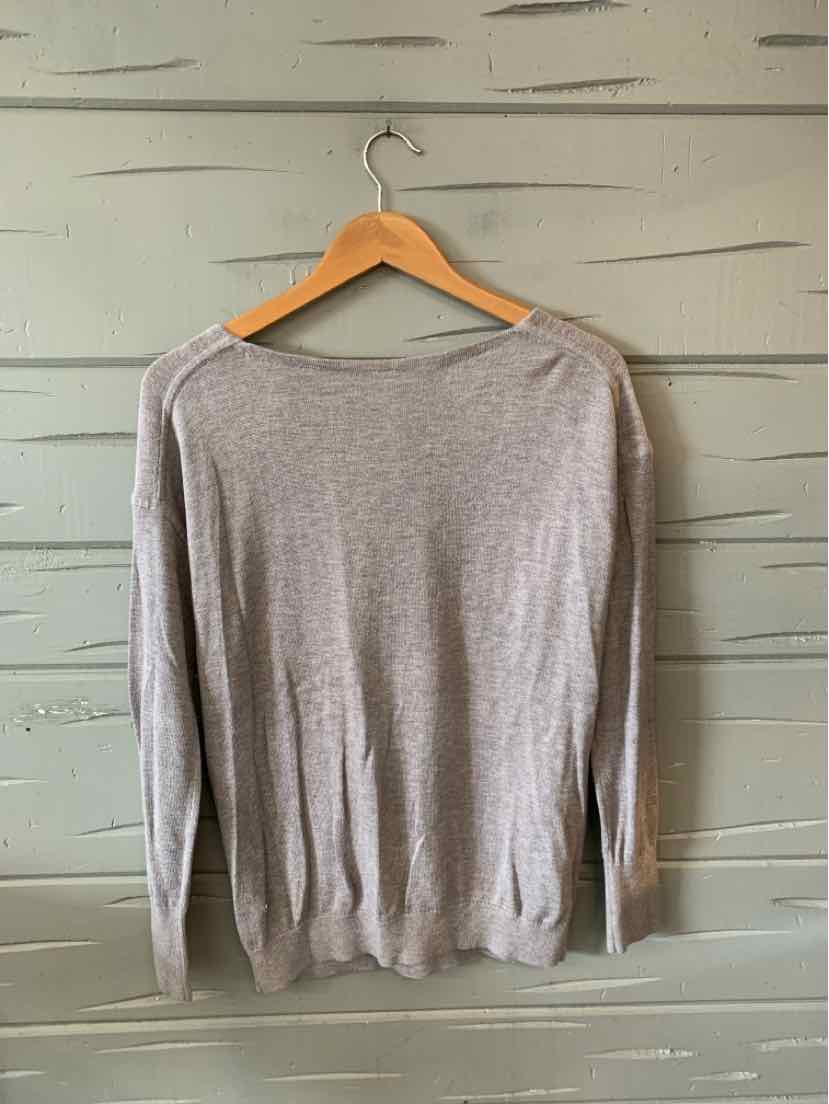 Light gray long-sleeve sweater with crew neckline hanging on wooden hanger against pale green wooden wall.