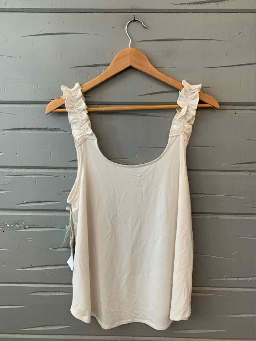 Cream-colored sleeveless top with ruffled straps on wooden hanger against gray wooden background.
