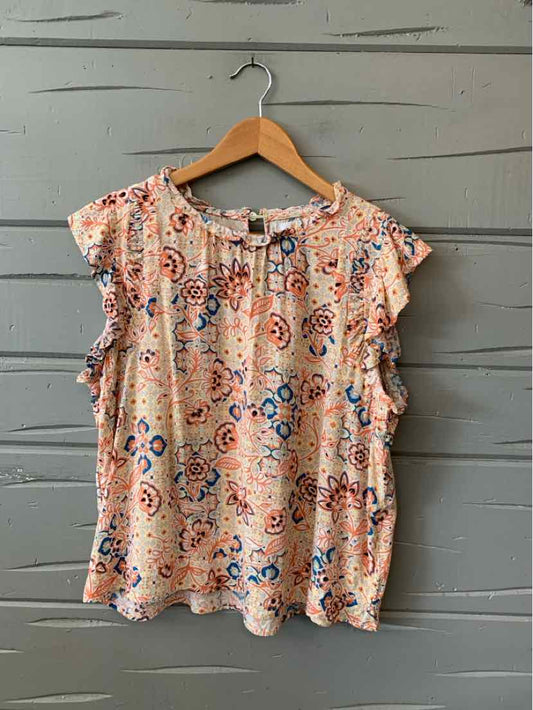Orange floral sleeveless blouse with ruffled trim and round neckline on wooden hanger.
