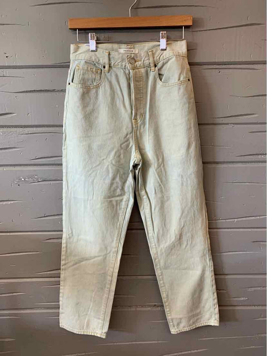 Light beige high-waisted denim jeans with five-pocket design hanging on wooden hanger against wooden wall.